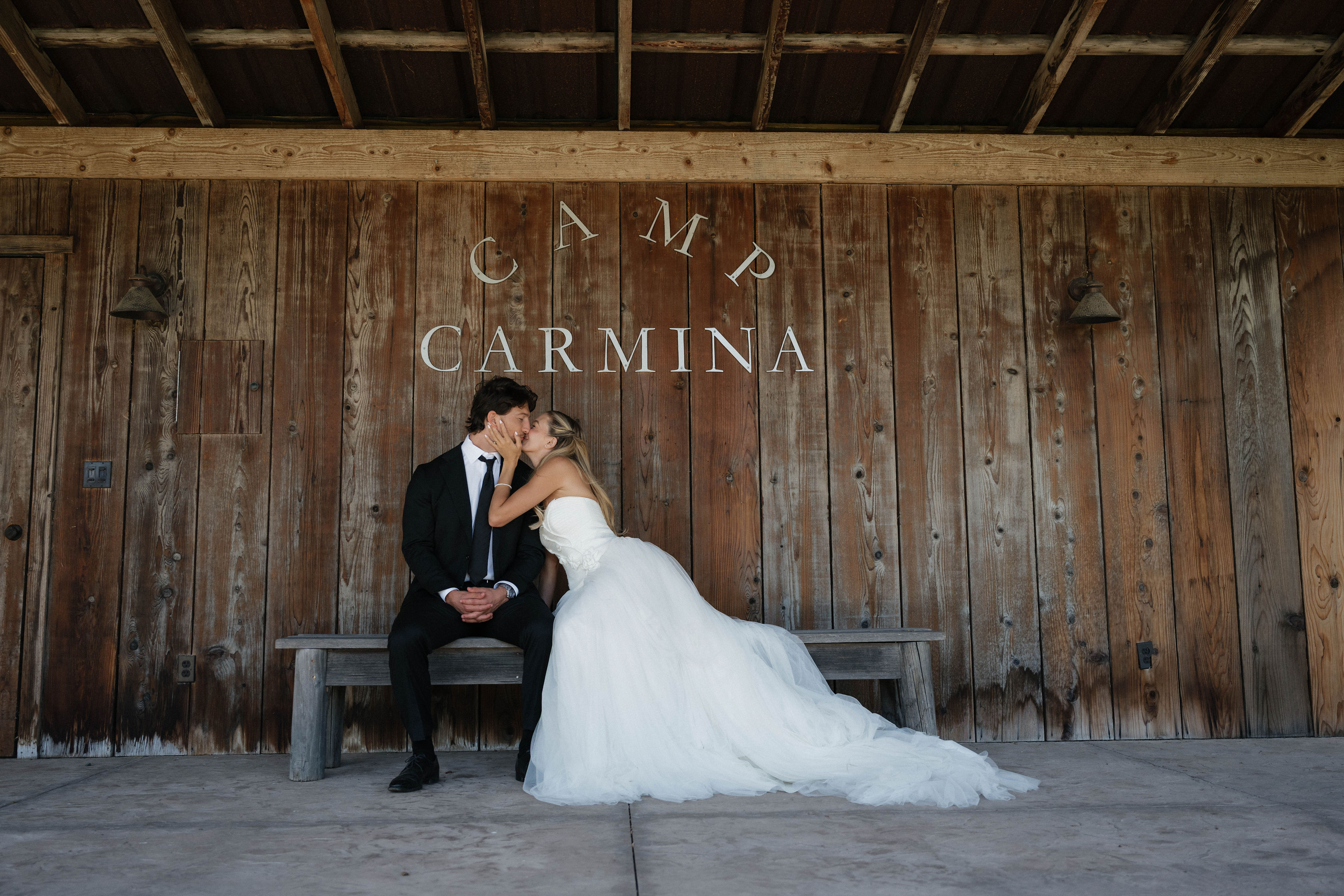 Bride and groom share a kiss under the camp carmina sign.