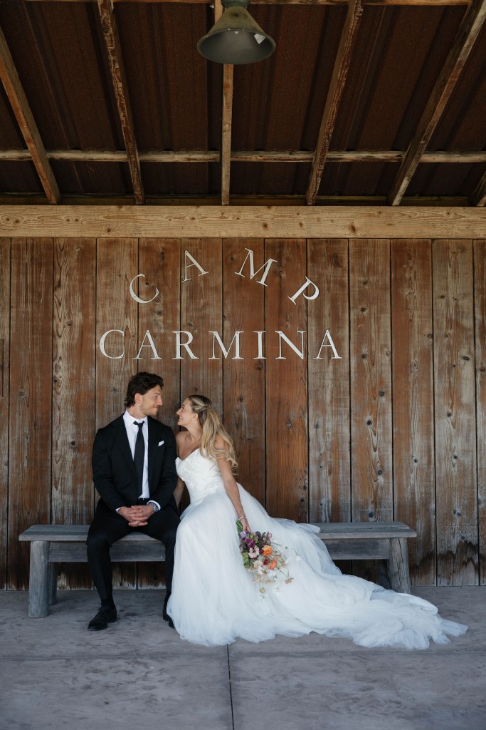 Bride and groom siting underneath the Camp Carmina sign on the outdoor stage.